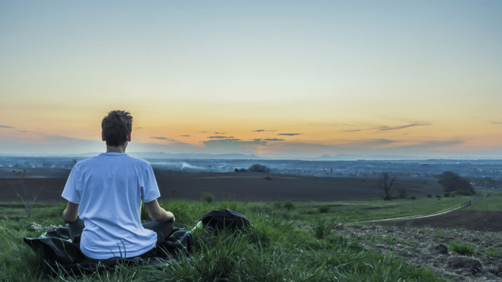 A person meditating on a dock in front of a lake