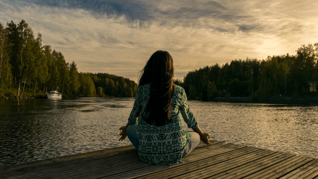 A person meditating on a dock in front of a lake