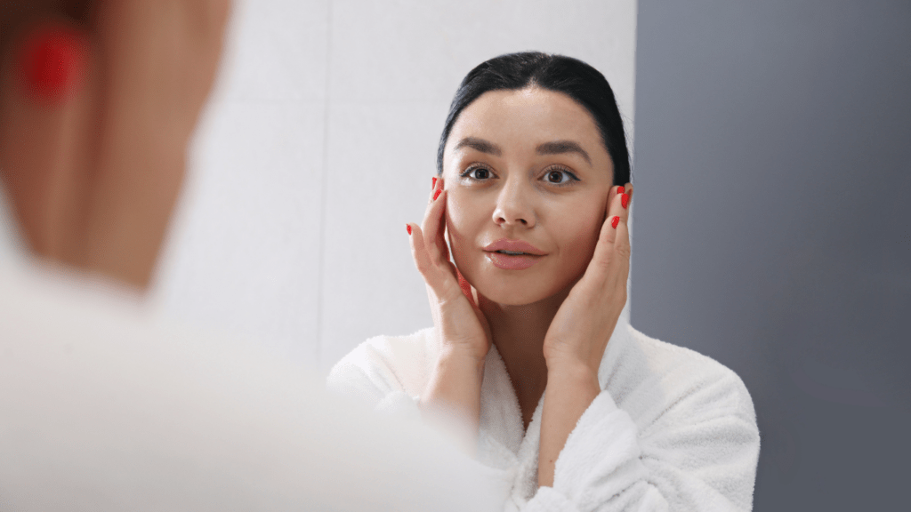 a person in a bathrobe looking at their face in the mirror