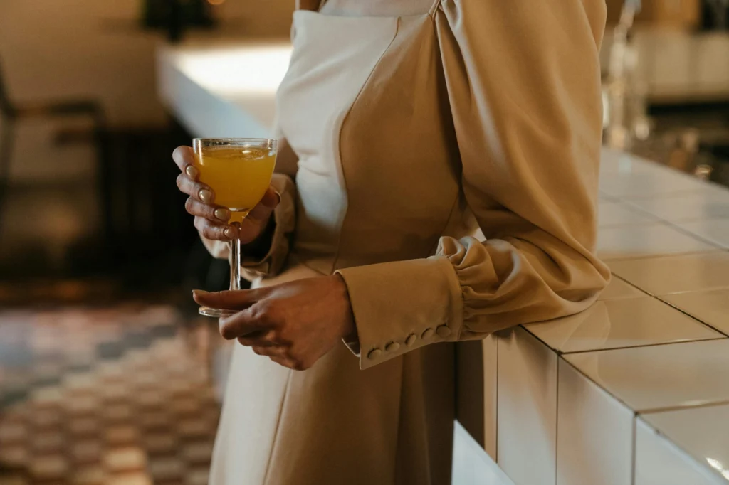 A woman in a stylish dress holding a cocktail at a bar counter, indoors.